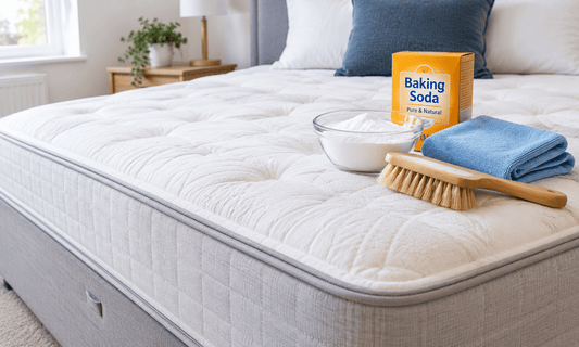 Stripped mattress on a divan base with a soft brush, microfibre cloth and baking soda ready for cleaning