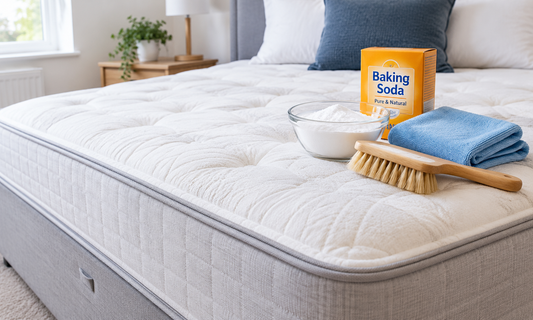 Stripped mattress on a divan base with a soft brush, microfibre cloth and baking soda ready for cleaning